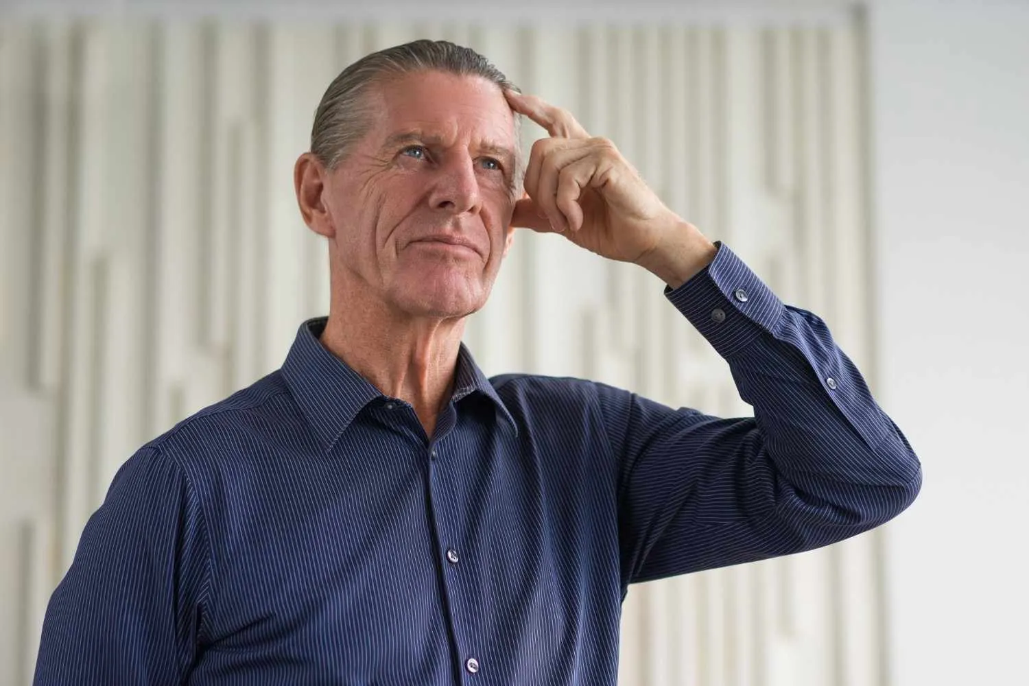 Thoughtful older man in a striped shirt touching his temple while he recalls something